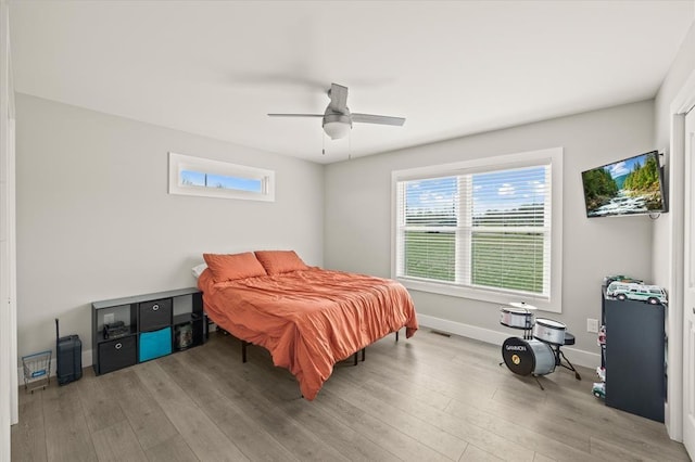 bedroom featuring baseboards, wood finished floors, multiple windows, and a ceiling fan