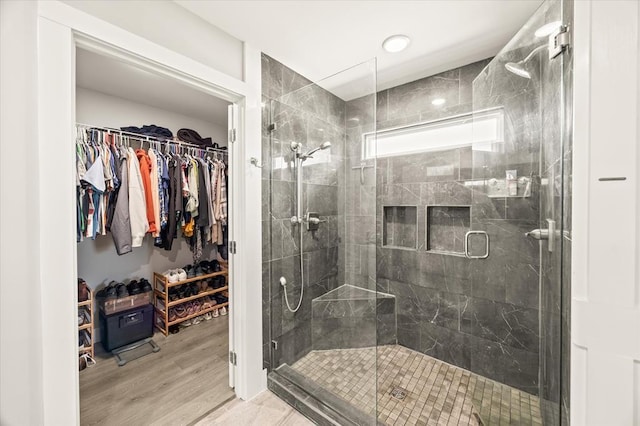 bathroom with a spacious closet, a shower stall, and wood finished floors