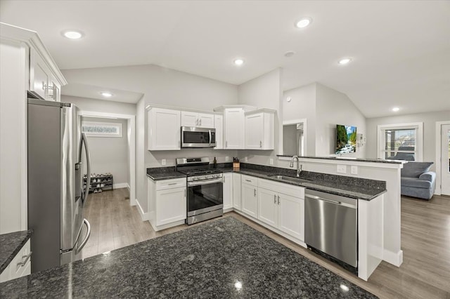 kitchen with appliances with stainless steel finishes, lofted ceiling, white cabinetry, a sink, and light wood-style floors