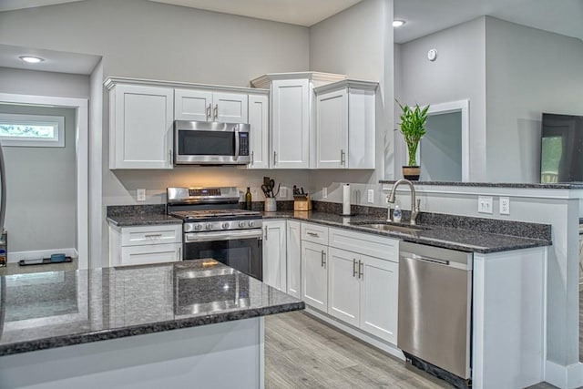 kitchen featuring white cabinets, light wood-style flooring, stainless steel appliances, dark stone counters, and a sink