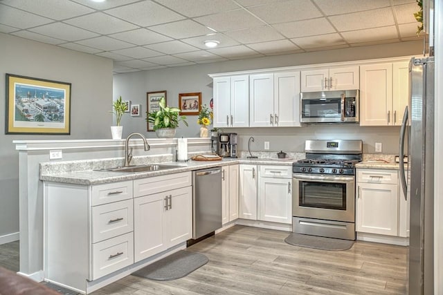 kitchen featuring a sink, a peninsula, light wood-style flooring, stainless steel appliances, and white cabinets