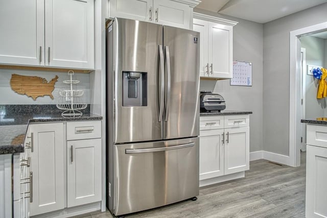 kitchen with stainless steel fridge with ice dispenser, white cabinetry, light wood-type flooring, dark stone countertops, and baseboards