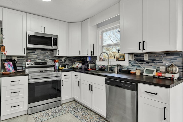 kitchen with white cabinetry, decorative backsplash, a sink, dark countertops, and appliances with stainless steel finishes