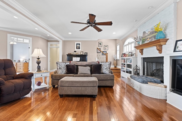 living area featuring crown molding, ceiling fan, hardwood / wood-style flooring, and a brick fireplace