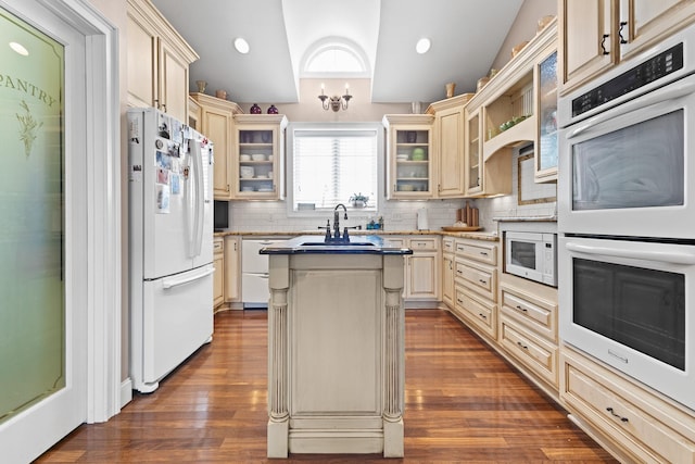 kitchen featuring backsplash, cream cabinets, an island with sink, and white appliances