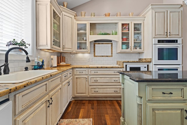 kitchen featuring decorative backsplash, dark wood-style flooring, white double oven, glass insert cabinets, and a sink