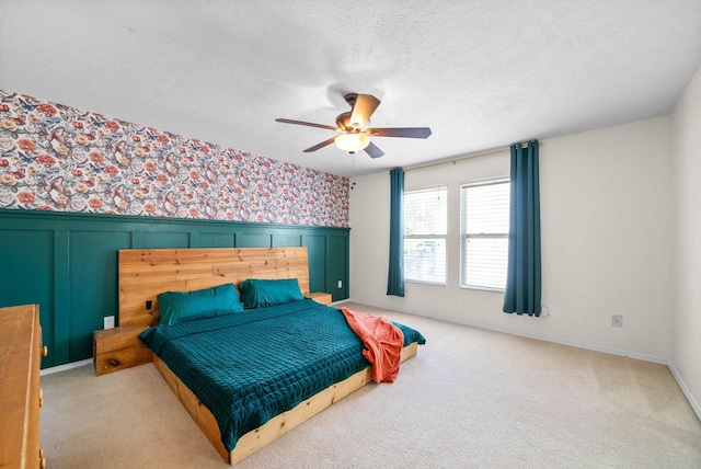 bedroom with carpet floors, a textured ceiling, wainscoting, wallpapered walls, and ceiling fan