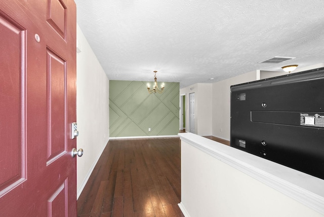 corridor with dark wood-style flooring, a textured ceiling, visible vents, baseboards, and an inviting chandelier