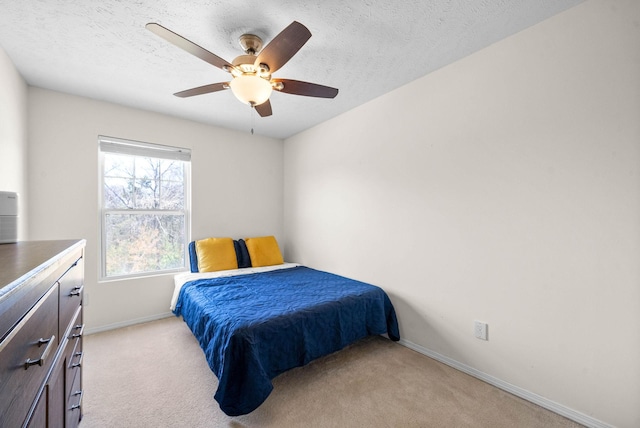 bedroom featuring light carpet, baseboards, a ceiling fan, and a textured ceiling