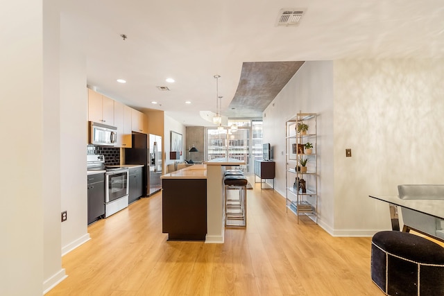 kitchen featuring visible vents, tasteful backsplash, appliances with stainless steel finishes, light wood-style floors, and a breakfast bar area