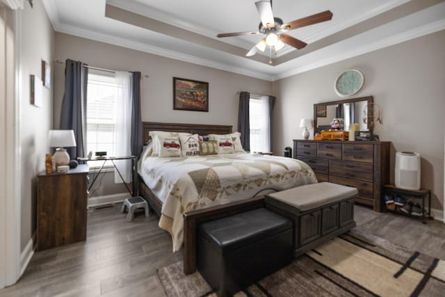 bedroom with baseboards, light wood-type flooring, crown molding, and a raised ceiling