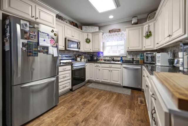 kitchen featuring a sink, stainless steel appliances, visible vents, decorative backsplash, and dark wood-style flooring