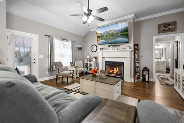 living area with a warm lit fireplace, ceiling fan, wood finished floors, and vaulted ceiling