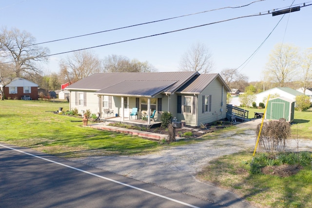 view of front facade with metal roof, an outbuilding, a storage unit, a front lawn, and covered porch