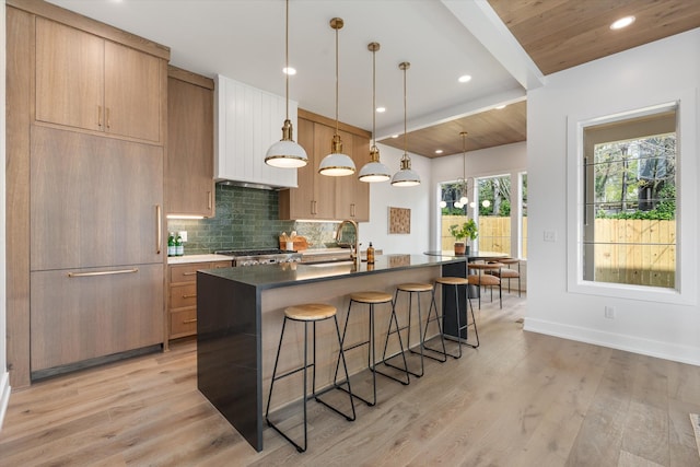 2510 Vaulx Ln, Nashville, TN 37204 - kitchen featuring light wood-type flooring, a breakfast bar, an island with sink, backsplash, and dark countertops