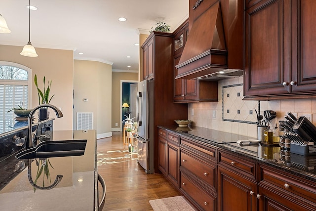 kitchen with visible vents, wood finished floors, premium range hood, a sink, and freestanding refrigerator