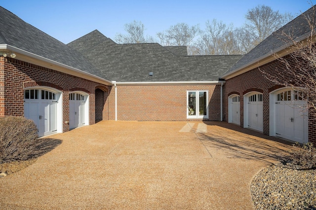 exterior space featuring brick siding, a shingled roof, concrete driveway, and a garage