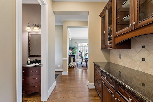 interior space with tasteful backsplash, ornamental molding, a sink, dark wood-style floors, and glass insert cabinets