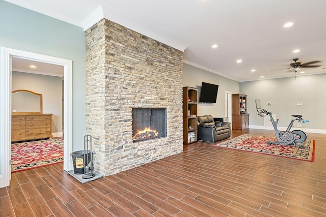 living area with a stone fireplace, crown molding, ceiling fan, and wood finish floors