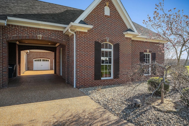 view of property exterior with driveway, brick siding, and a shingled roof