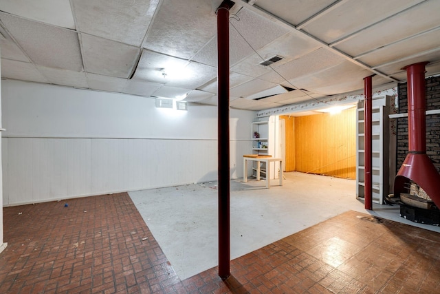 finished basement with visible vents, a drop ceiling, and a wainscoted wall