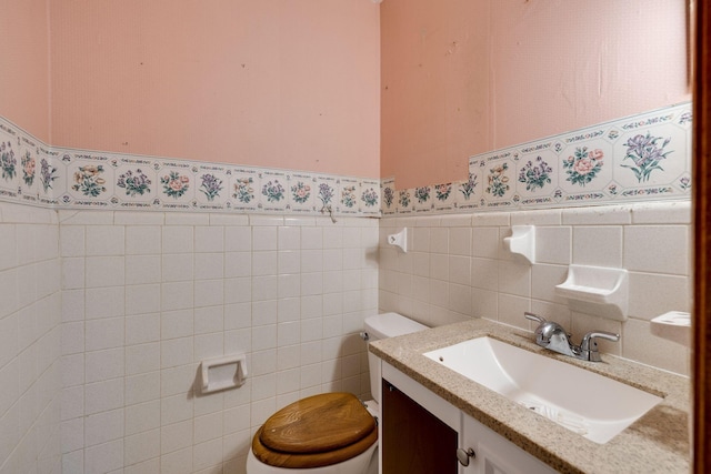 half bath with toilet, vanity, wainscoting, wallpapered walls, and tile walls
