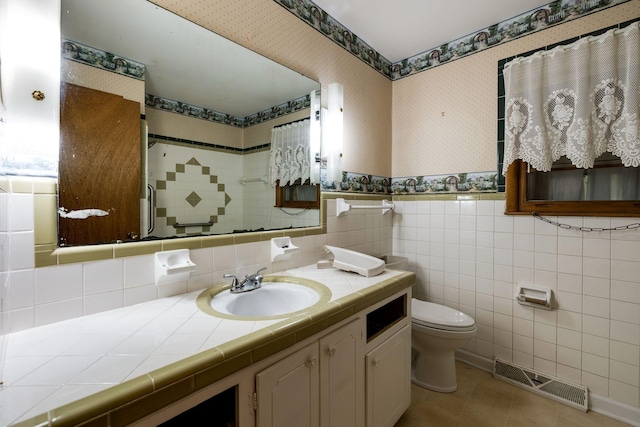 full bath featuring toilet, tiled shower, visible vents, wallpapered walls, and tile walls