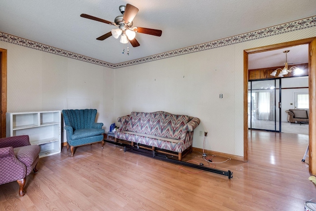 living area featuring ceiling fan with notable chandelier, wood finished floors, and baseboards