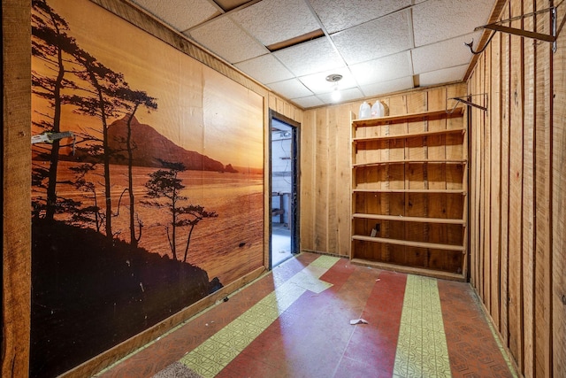 interior space featuring a drop ceiling, tile patterned floors, and wooden walls