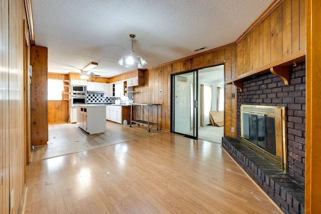 kitchen featuring a fireplace, visible vents, wooden walls, and light wood finished floors