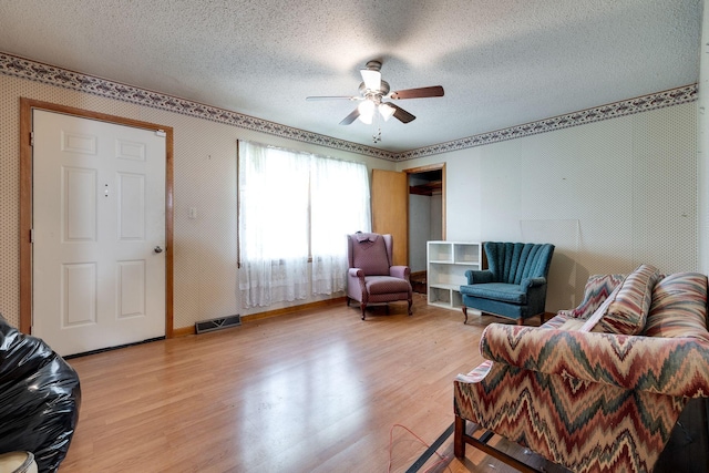 living area with a textured ceiling, visible vents, light wood finished floors, baseboards, and a ceiling fan