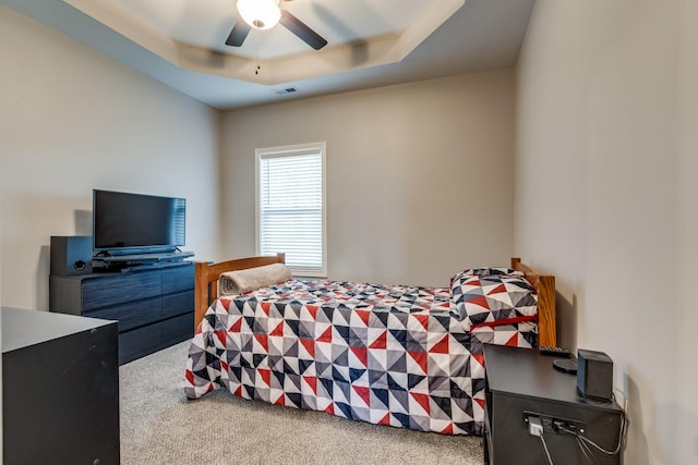 carpeted bedroom with visible vents, a ceiling fan, and a raised ceiling