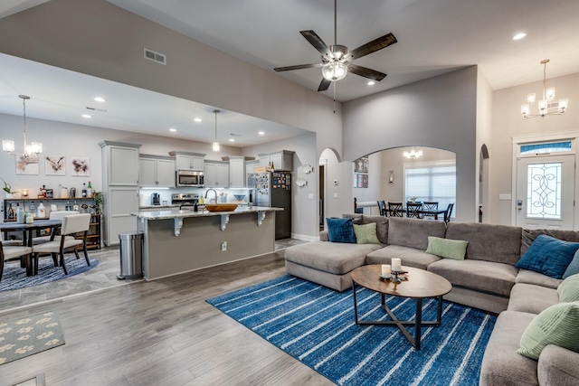 living room with recessed lighting, ceiling fan with notable chandelier, arched walkways, light wood finished floors, and visible vents