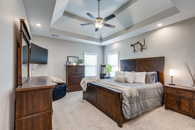 bedroom with a raised ceiling, ceiling fan, light colored carpet, and visible vents