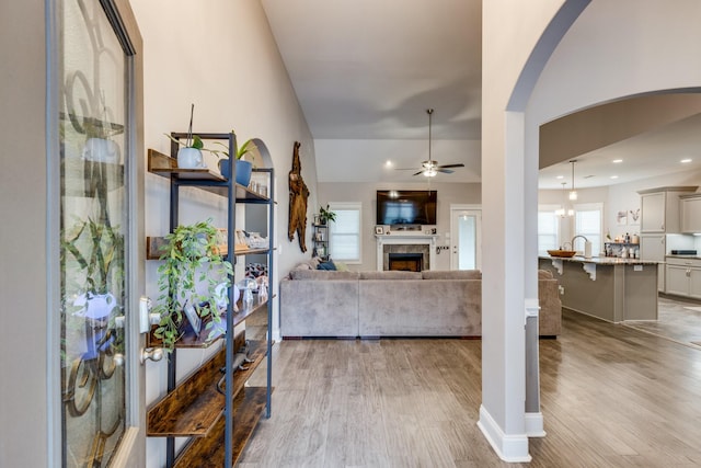 interior space featuring a fireplace, ceiling fan, recessed lighting, arched walkways, and light wood-type flooring