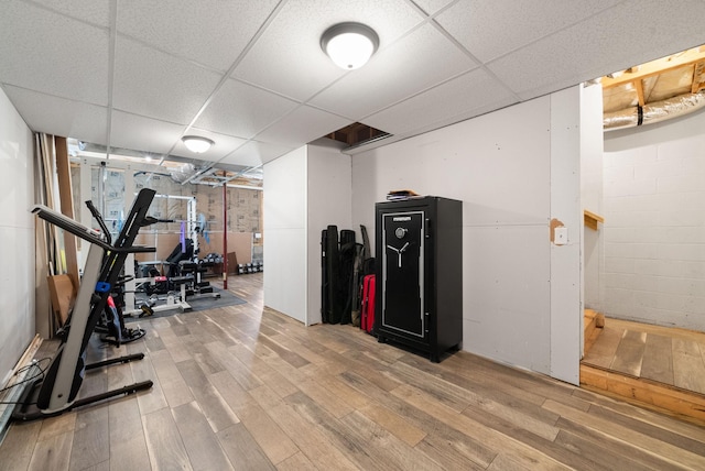 workout room featuring a drop ceiling, concrete block wall, and wood finished floors
