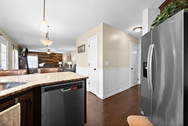 kitchen featuring dark wood finished floors, appliances with stainless steel finishes, light stone counters, pendant lighting, and wainscoting