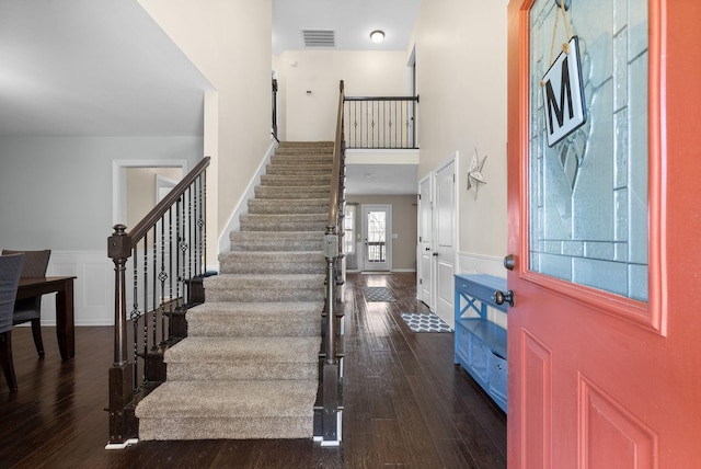 foyer entrance with a wainscoted wall, stairs, a high ceiling, dark wood finished floors, and visible vents