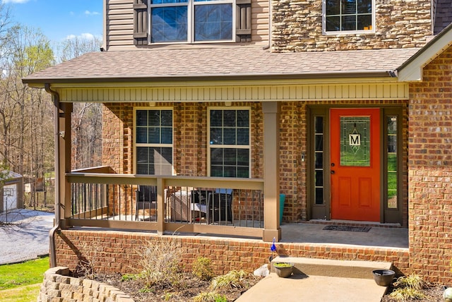 entrance to property with brick siding, a porch, and roof with shingles