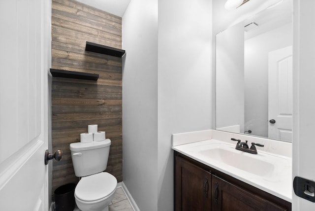 half bathroom featuring toilet, vanity, wooden walls, and visible vents