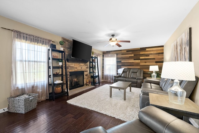 living area featuring wooden walls, a fireplace, a ceiling fan, dark wood finished floors, and an accent wall