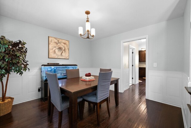 dining area with an inviting chandelier, a wainscoted wall, a decorative wall, and dark wood finished floors