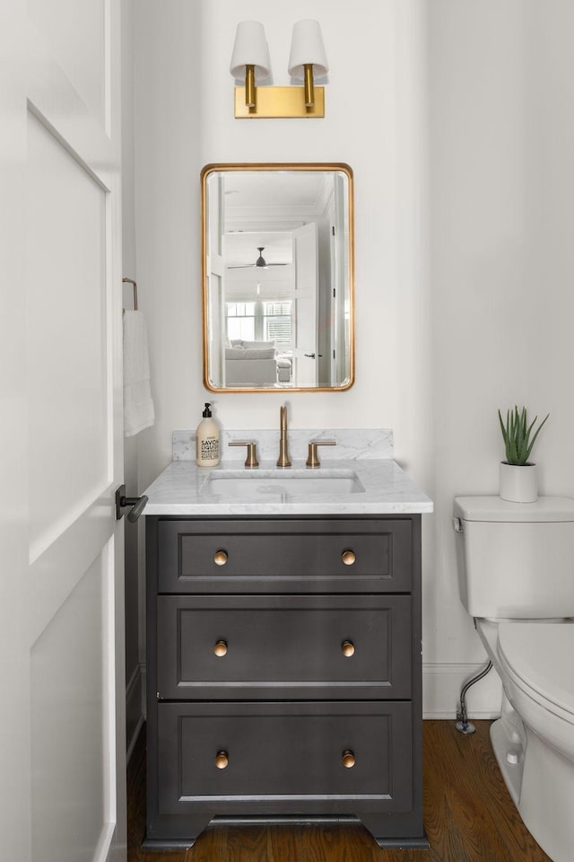half bath with baseboards, wood finished floors, toilet, and vanity
