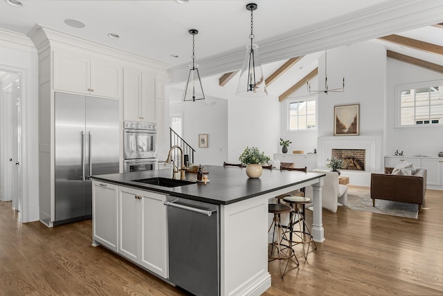 kitchen with white cabinets, a fireplace, stainless steel appliances, dark countertops, and a sink