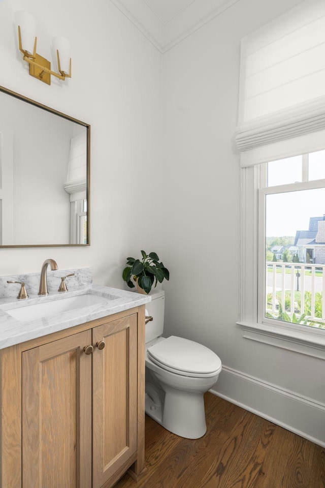 half bathroom featuring baseboards, ornamental molding, toilet, wood finished floors, and vanity