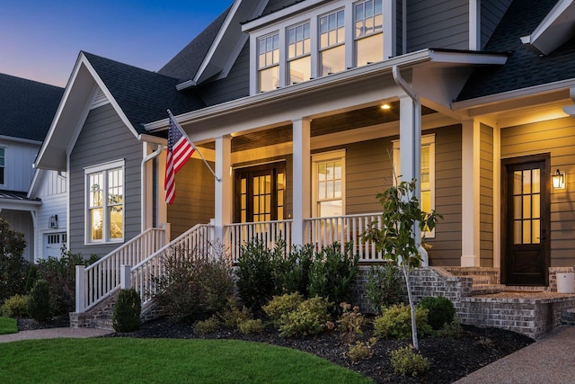 exterior entry at dusk featuring a porch and roof with shingles