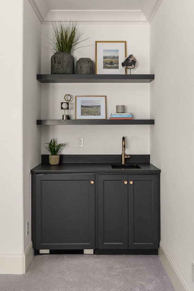 bar featuring crown molding, a sink, indoor wet bar, baseboards, and light colored carpet