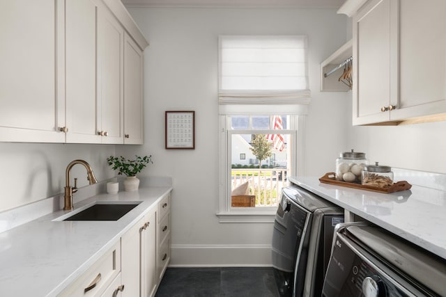 clothes washing area with independent washer and dryer, a sink, cabinet space, and baseboards