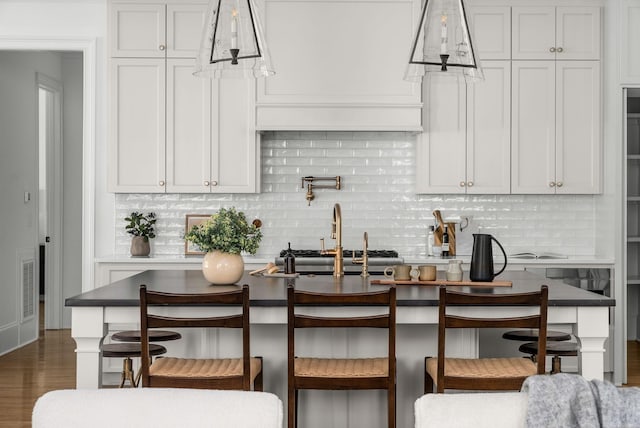 kitchen featuring a kitchen bar, dark wood-type flooring, backsplash, hanging light fixtures, and visible vents