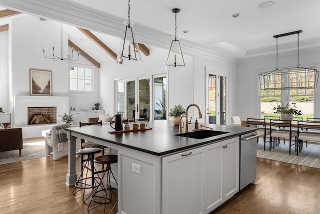 kitchen featuring stainless steel dishwasher, dark countertops, a sink, and a chandelier